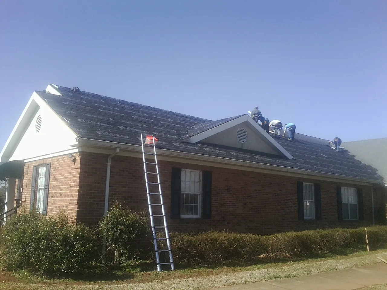 Crew tearing shingles off a brick ranch roof with a ladder set — Emergency Roof Repair work by our crew in Oldtown