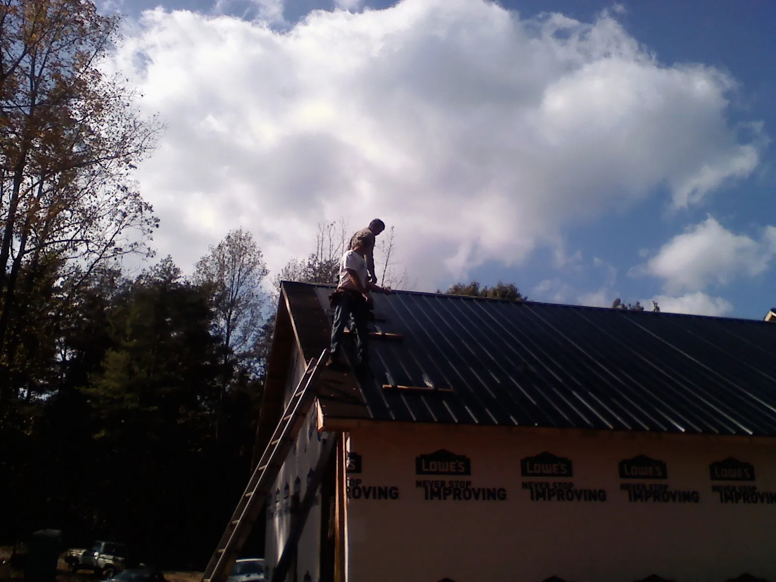 Roofer fastening dark metal panels high against a cloudy sky, from a Roof Inspection job in Oldtown
