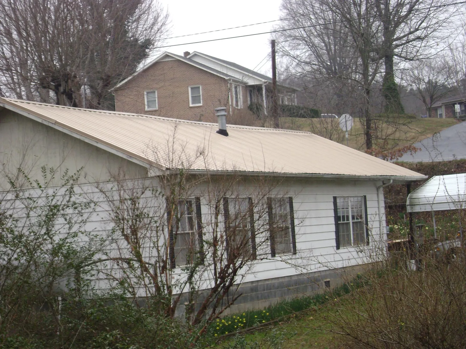 Tan metal roof on a white sided house set into a hillside — Commercial Roofing by Roofing Brothers in Oldtown
